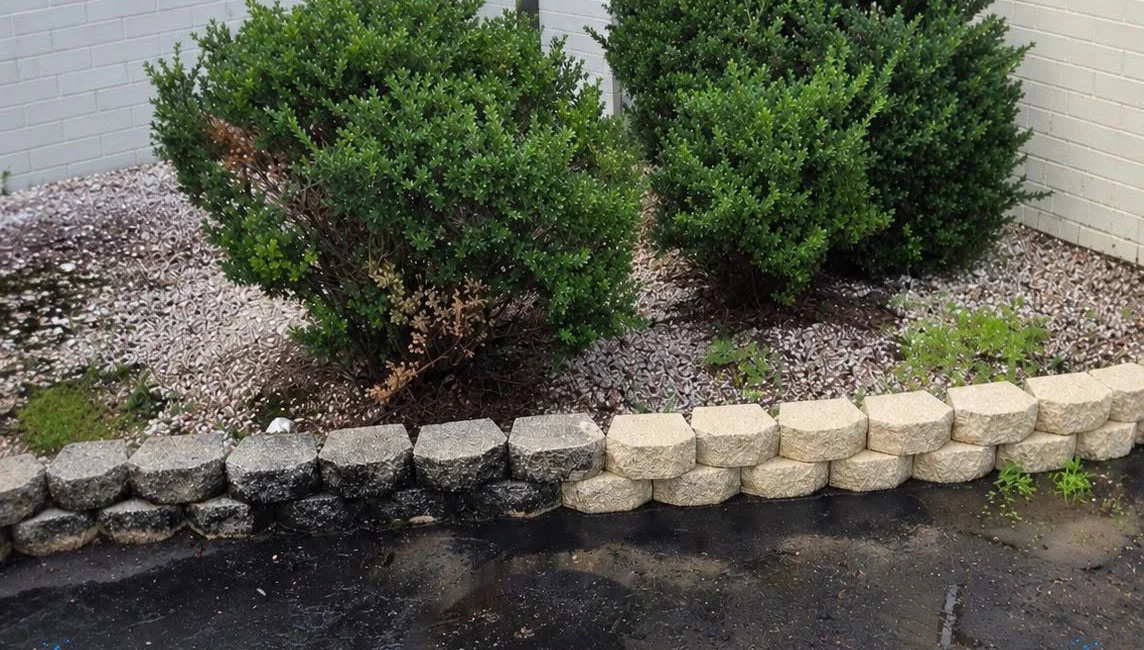 A block retaining wall, left half still dark with grime and right half washed back to its original tan color